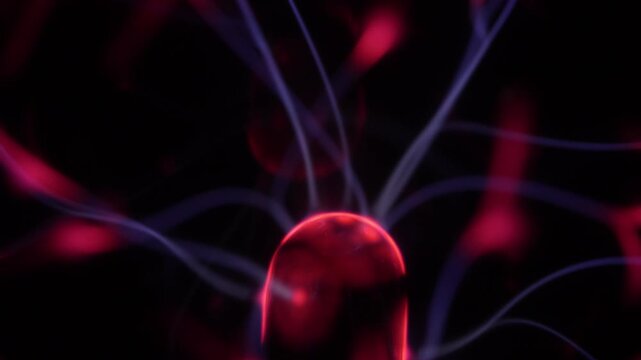 Close-up of a plasma ball coil. The plasma ball creates beams of energy in red and purple.