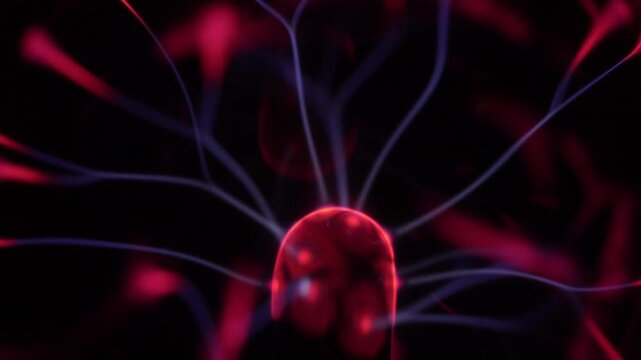 Close-up of a plasma ball coil. The plasma ball creates beams of energy in red and purple.