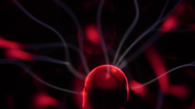 Close-up of a plasma ball coil. The plasma ball creates beams of energy in red and white.