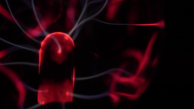 Close-up of a plasma ball coil. The plasma ball creates red and white energy beams. The coil is on the right.