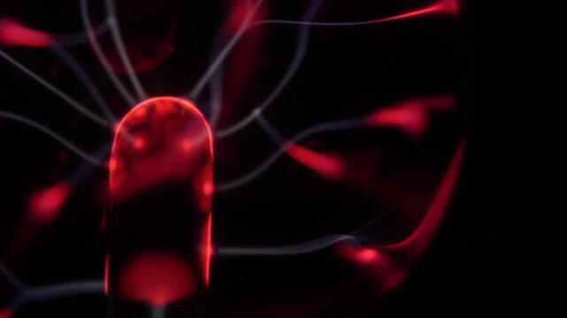Close-up of a plasma ball coil. The plasma ball creates red and white energy beams. The coil is on the left.