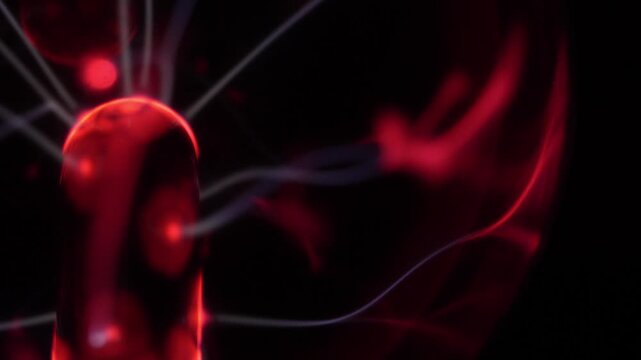 Close-up of a plasma ball coil. The plasma ball creates red and white energy beams. The coil is on the left.