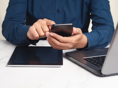 Person Using Smartphone with Laptop and Tablet at Desk