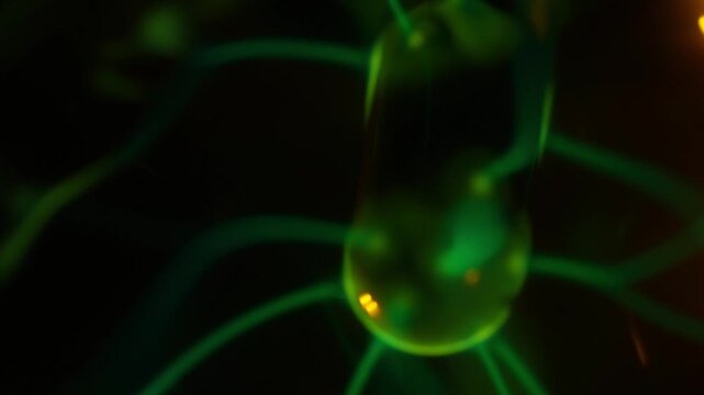 A close-up of the working coil of a plasma ball, which creates green electrical discharges. A warm beam of light illuminates the interior of the plasma ball in the beam.