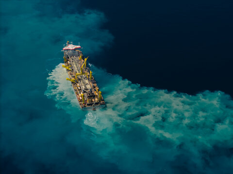 Aerial view of a trailing suction hopper dredger ship creating a large plume of sediment in the deep blue ocean near Dhidhdhoo, Thiladhunmathee Uthur, Maldives.