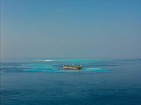 Aerial view of a large dredging ship operating in the turquoise waters of the Indian Ocean near the coast of Dhidhdhoo, Thiladhunmathee Uthur, Maldives.