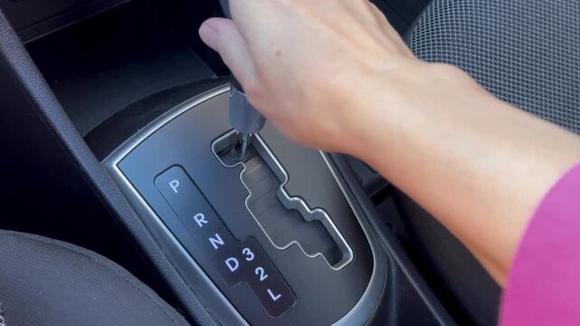 Woman hand holding automatic gear shift lever inside car, close-up of transmission selector on center console, vehicle interior, driving, transport.