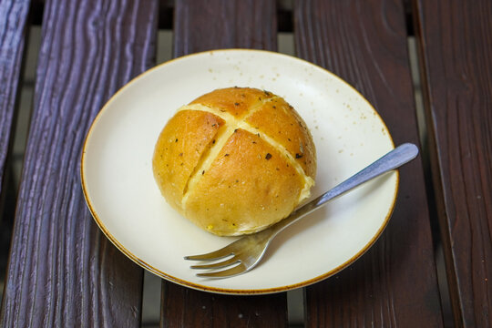 Freshly baked garlic cheese bun with melted cheese filling and aromatic herbs, served on a white ceramic plate as a savory bakery snack.