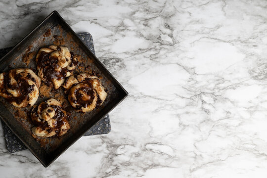 Small batch chocolate cinnamon buns, knots, or twist freshly baked, vintage baking pan on marble background.