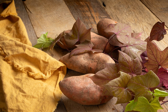Sweet potatoes on rustic wooden surface with leaves and vine