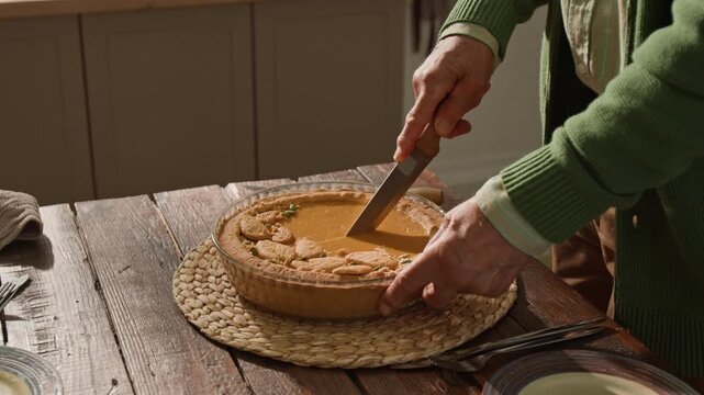 Unrecognizable senior man cutting freshly baked pumpkin pie on rustic wooden table. Clip is suitable for Thanksgiving marketing campaigns, holiday cooking promos, and family lifestyle ads