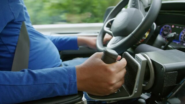 Driver with a physical impairment using assistive technology on a car dashboard and adaptive hand controls for safe and comfortable driving.