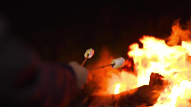 Person roasting marshmallows over a campfire at night