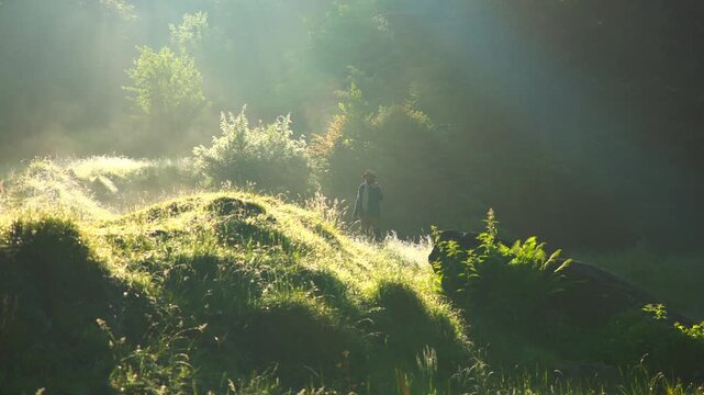 Hiker exploring a misty forest with sunbeams shining through