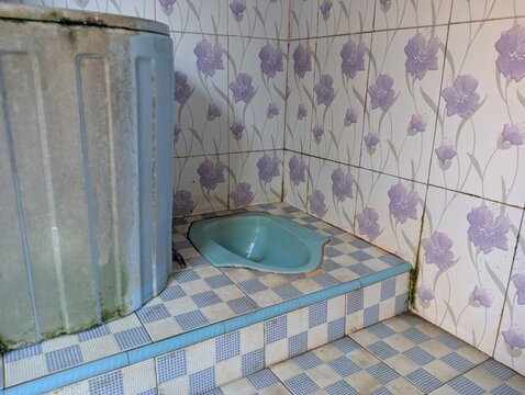 Traditional Asian squat toilet with blue water tub and floral wall tiles in a simple bathroom.