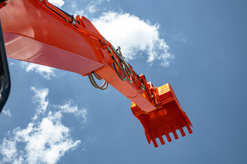 Orange excavator boom and arm with bucket raised against sky. Modern construction machinery earthmoving mechanism perspective view with hydraulic hoses and industrial transport vehicle details. © NastyaPhoto