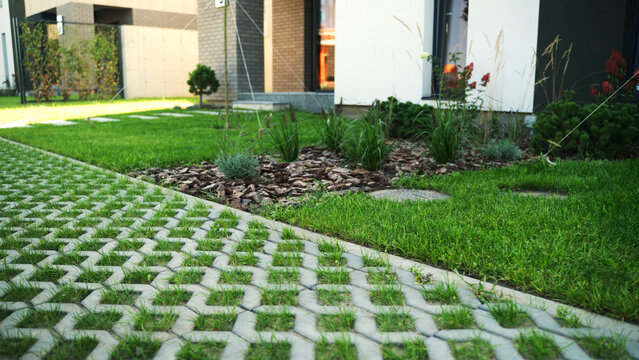Modern residential garden design featuring a green lawn, eco-friendly grass paving, wood chips, and various plants