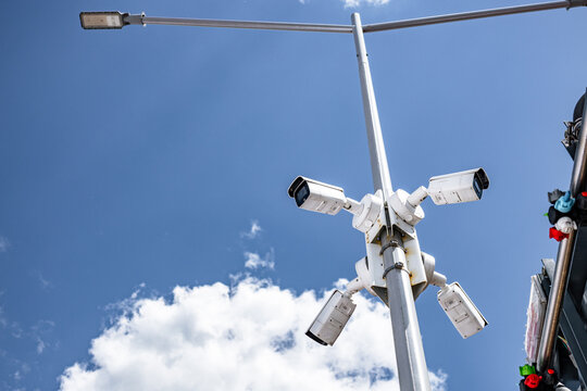 Outdoor CCTV security cameras mounted on street light pole. Modern city surveillance public safety system against blue sky background with municipal monitoring technology details view.