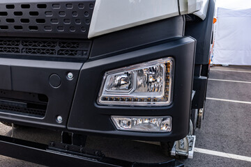 Semi truck front LED headlight block with fog light lens. Commercial vehicle white plastic bumper shell detail view with radiator grill panel and long haul transport tractor engineering details. © NastyaPhoto