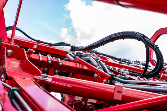 Agricultural machinery hydraulic pressure lines and hoses block. Modern farm equipment crop harvesting section on red metal frame with sky background and engineering technical details view.