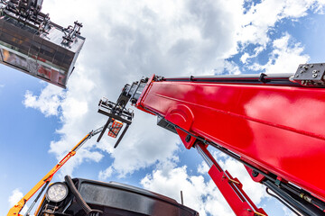 Red telehandler telescopic boom raised high against sky. Modern construction lifting machinery perspective low angle view with aerial work platform basket and industrial equipment details. © NastyaPhoto