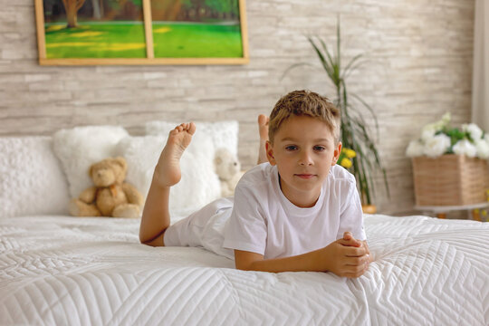 Cute little preschool child, cute blond boy, playing in bed with many teddy bears, handmade amigurumi toys, enjoying toy game