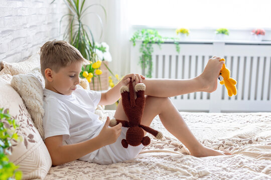 Cute little preschool child, cute blond boy, playing in bed with many teddy bears, handmade amigurumi toys, enjoying toy game