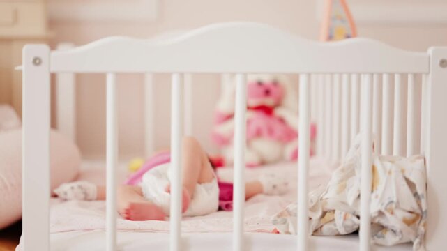 Baby sleeping peacefully in white wooden crib inside nursery bedroom during daytime.
