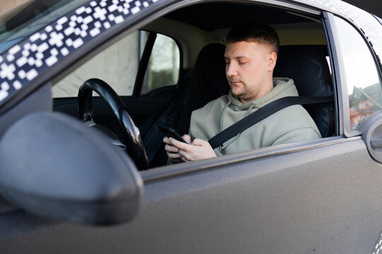  Man sitting in car with seatbelt fastened using smartphone, distracted driving and mobile communication concept.