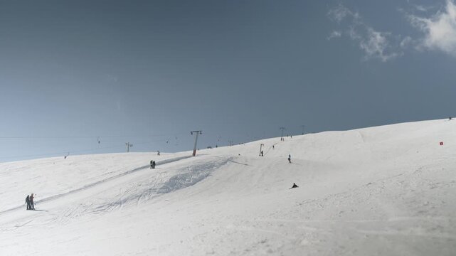People are skiing and snowboarding down a snow-covered mountain slope on a sunny winter day. Ski lifts are visible in the background as recreational activities take place.
