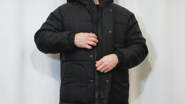 A man is unfastening the buttons and zip on his black winter jacket it is a black jacket with button fastenings. Taking off a man&rsquo;s jacket.