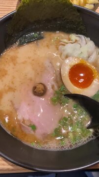 Delicious bowl of ramen featuring sliced chashu pork, soft-boiled egg with runny yolk, green onions, nori seaweed and noodles in rich broth. Authentic Japanese noodle soup close-up.