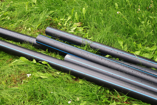 Plastic pipes on the grass. A pile of gray water pipes lies on the ground, pipes in the yard.