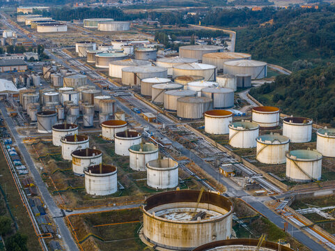 Aerial view of the fuel depot with numerous large cylindrical oil storage tanks arranged in rows, surrounded by industrial infrastructure and green hills in Rome, Lazio, Italy.