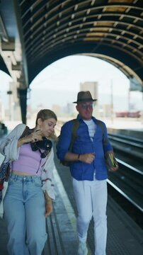 Two tourists anxiously hurry across a train station platform, possibly having missed their train. A couple of travelers look confused and a bit frustrated while waiting on the railway station.
