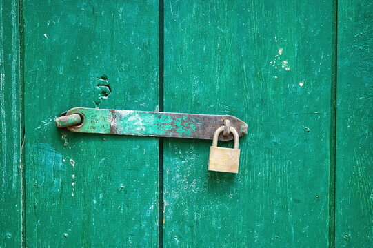 Vecchio lucchetto in ottone chiuso su un chiavistello di un portone in legno verde