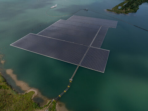Aerial view of a large floating solar farm on a calm lake, featuring rows of photovoltaic panels connected by a walkway to the shoreline in the Netherlands.