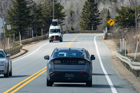 Quebec, Canada, 24 April 2026 : A grey Nissan Leaf electric car drives on a winding road with other vehicles and trees.