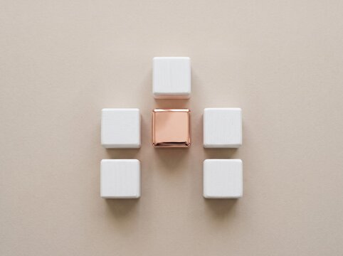Symmetrical flat lay of five white wooden blocks surrounding a polished rose gold cube, representing modular flexibility, customization, and adaptable design