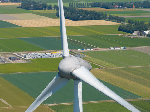 Aerial view of a large wind turbine set against a vast patchwork of green agricultural fields and rural farmland, Netherlands.