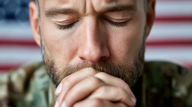Static close up of male soldier praying with hands clasped in front of american flag in indoor patriotic setting