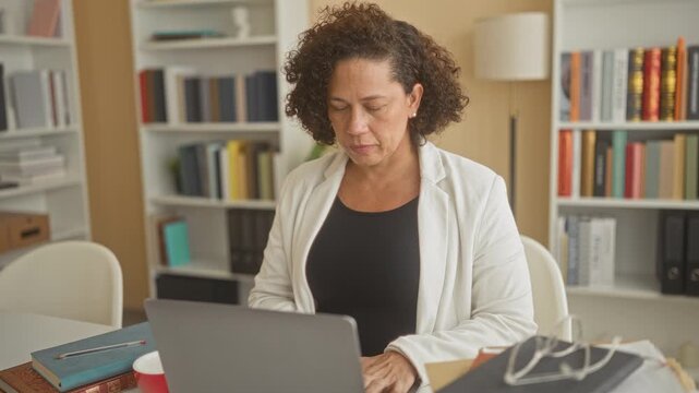 Woman working at laptop, smiling and forming a heart shape with her hands while seated at a desk in a building; warmth connection.