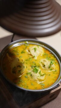 Vertical video close up of steaming hot indian curry dish with kofta dumplings garnished with coriander