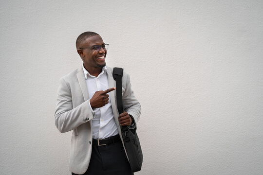 African american businessman working as CFO, pointing toward background, holding bag, isolated studio background. Black business man smiling, focused on daily tasks, managing accounts. Copy space