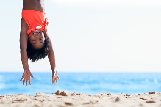 Hanging, smile and portrait of black child at beach for summer vacation, freedom and travel. Holiday getaway, excited and weekend break with kid upside down for adventure, fun and playful space