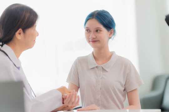 Female doctor explaining spine model to a young patient with blue hair in a clinic, medical consultation about back pain or posture correction.