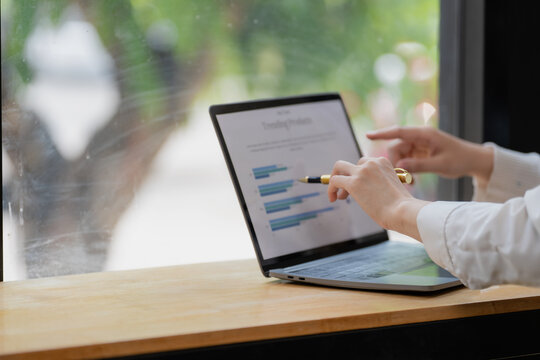 Businesswoman holding pen and pointing at graph data chart on laptop screen for market analysis.
