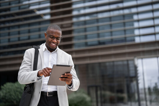 Accountant, african businessman, using tablet, browsing report, outdoor near office building. Black business man smiling, focused on daily tasks, building strong client partnerships. Copy space