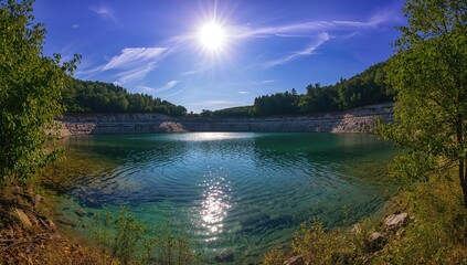 Fototapeta premium Mountain Lake Surrounded by Lush Greenery Under Bright Sunlight