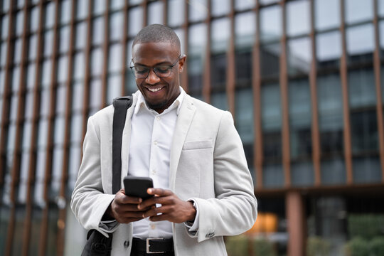 Portrait of african american businessman, marketing manager, using smartphone, checking email, outdoor near office building. Black business man smiling, managing work remotely, managing accounts.